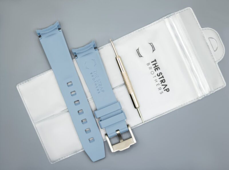 Achterkant van het lichtblauwe MoonSwatch horlogebandje en de verpakking van The Strap Brothers