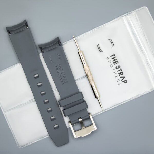 Achterkant van het grijze MoonSwatch horlogebandje en de verpakking van The Strap Brothers