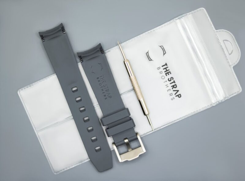 Achterkant van het grijze MoonSwatch horlogebandje en de verpakking van The Strap Brothers