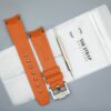 Achterkant van het oranje MoonSwatch horlogebandje en de verpakking van The Strap Brothers