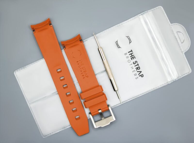 Achterkant van het oranje MoonSwatch horlogebandje en de verpakking van The Strap Brothers