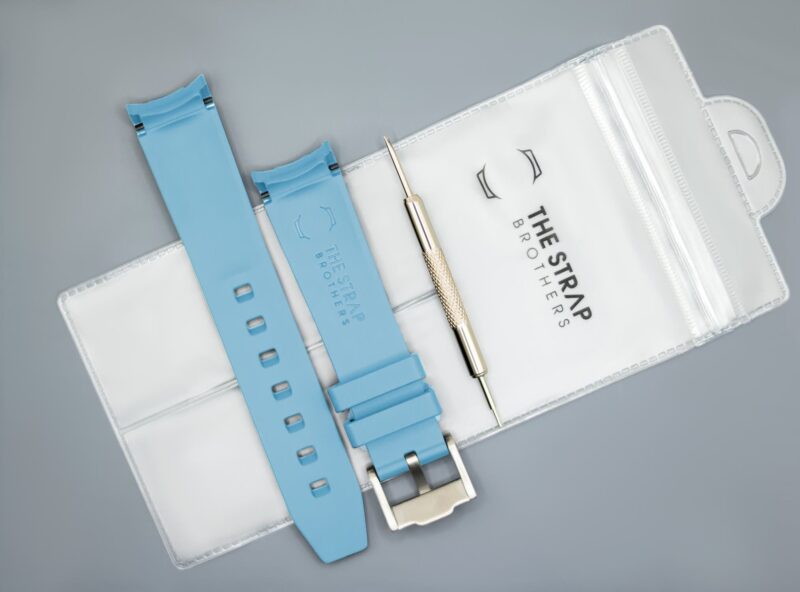 Achterkant van het hemelsblauwe MoonSwatch horlogebandje en de verpakking van The Strap Brothers